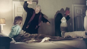 Medium shot of Max Von Sydow as Father Merrin, arm raised, Jason Miller as Father Damien Karras, facing wall and Linda Blair as Regan MacNeil sitting up in bed during exorcism.